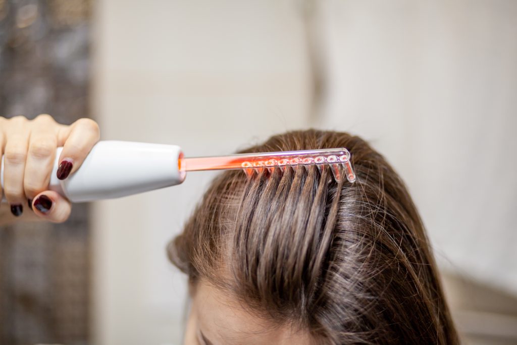 Woman uses darsonval for massage head's skin. Receiving electric darsonval facial massage procedure. Face Beauty Treatment. Darsonval Therapy Using High Frequency D'Arsonval, Skin Care Device .