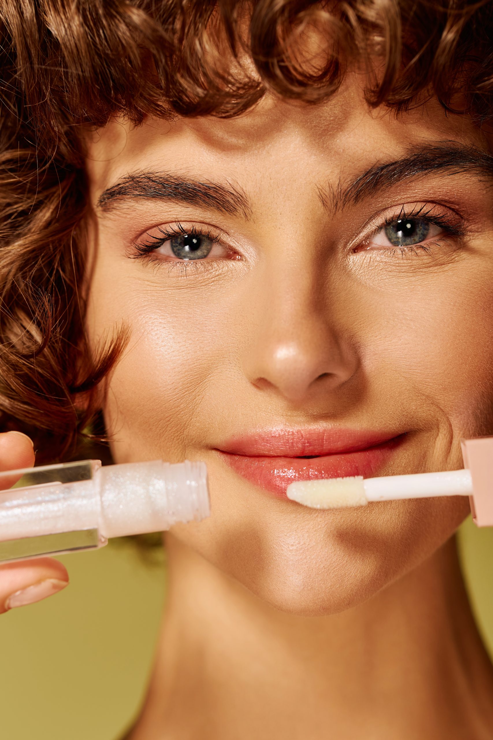 Lip Care Routine. A young woman smiles brightly as she applies lip gloss, radiating happiness and confidence.