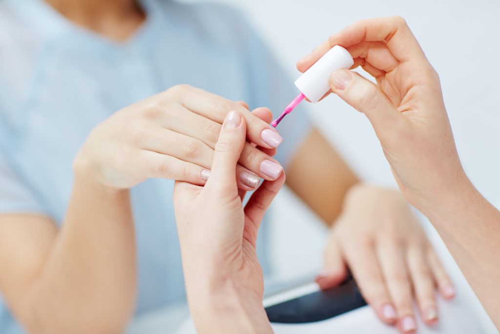 Nail Maintenance Routine. Manicurist applying nail polish on female fingernails in beauty salon.
