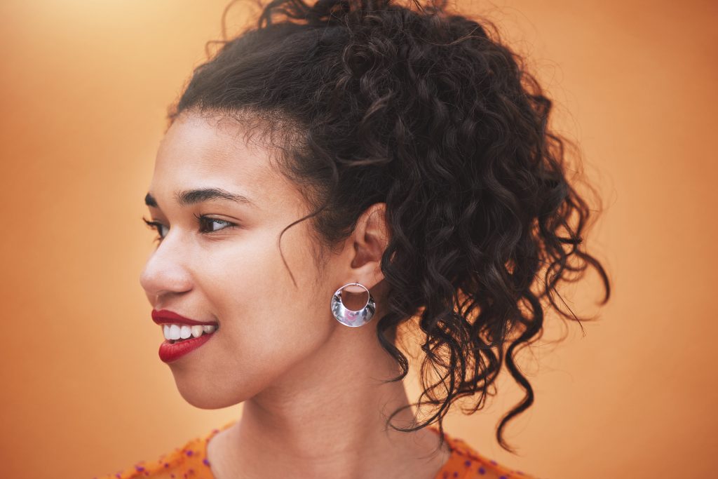 Closeup beautiful mixed race fashion woman looking thoughtful and smiling against an orange wall ba.