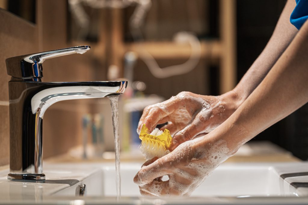 Closeup view of a woman washing her hands thoroughly with soap and brush at home in her bathroom.