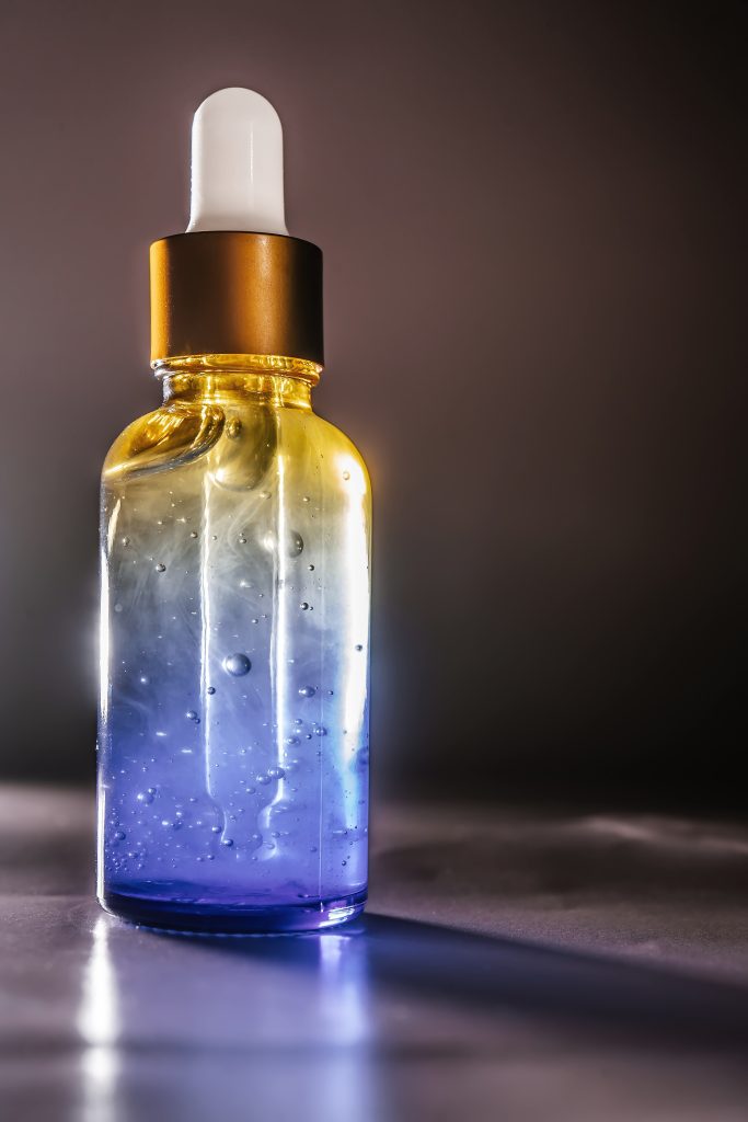Eyebrow Growth Serums. Cosmetic bottle with water splashes on a dark background. Front view. Perfectly emphasizes the moisturizing function of the serum.