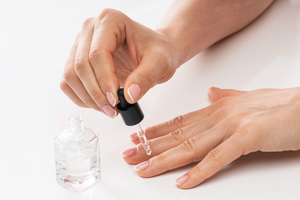 Female hands and bottle of nourishing cuticle oil with a dropper on white background
