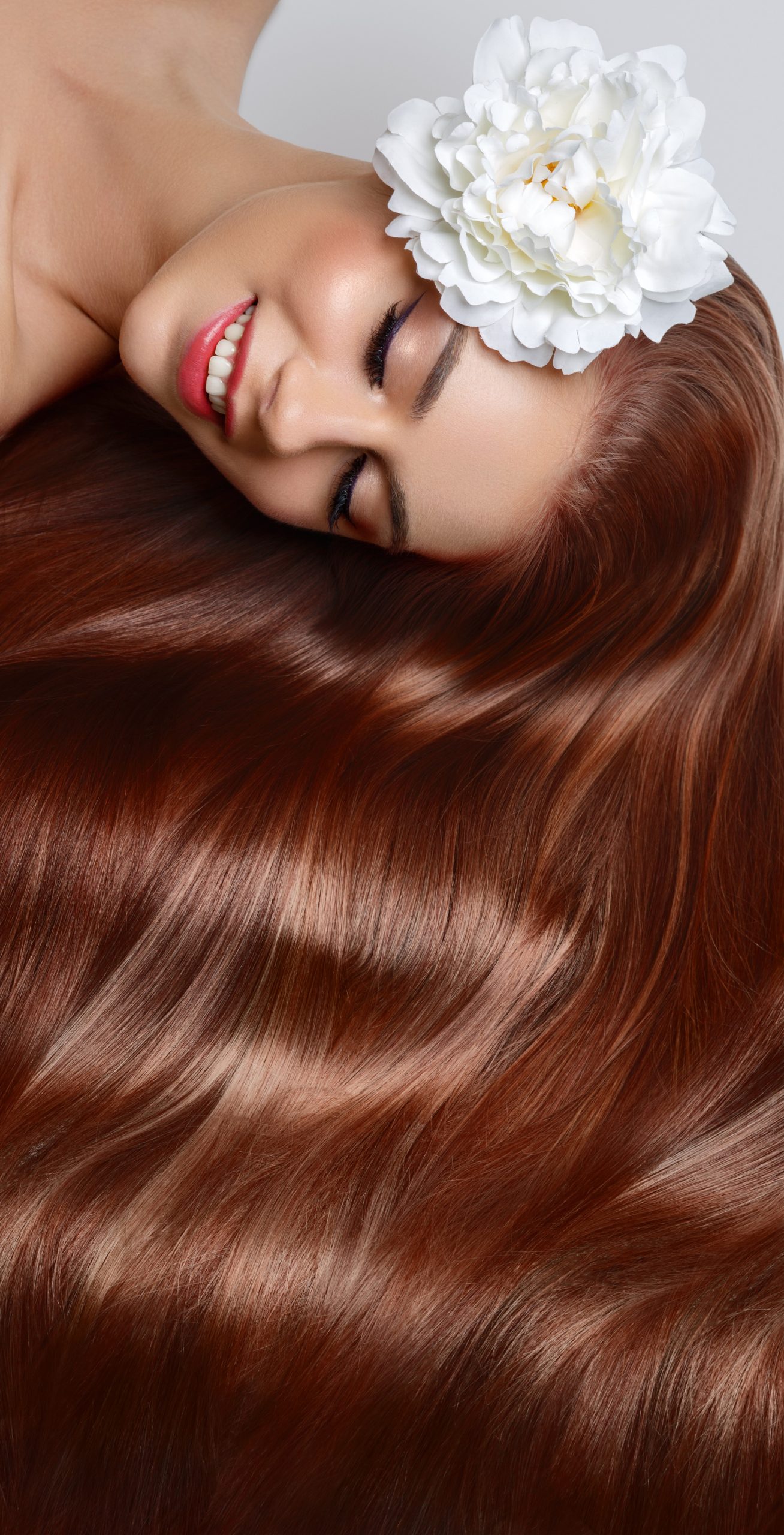 Hair Gloss Treatments. beautiful young woman with long healthy shiny hair and flower in it. red color. eyes closed. studio beauty shot. copy space.