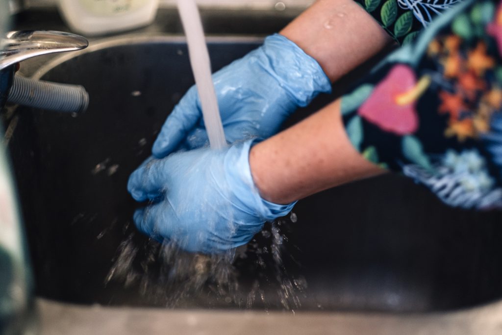 hands in latex gloves washed under running tap water. Manicurist applying nail polish on female fingernails in beauty salon.