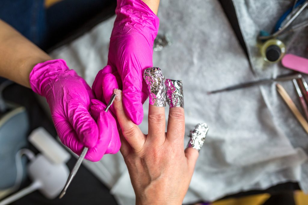 manicure master in pink gloves scraping off the old coat of varnish in manicure salon using drill. Professional manicure in cosmetology clinic. Hygiene for feet in beauty salon.