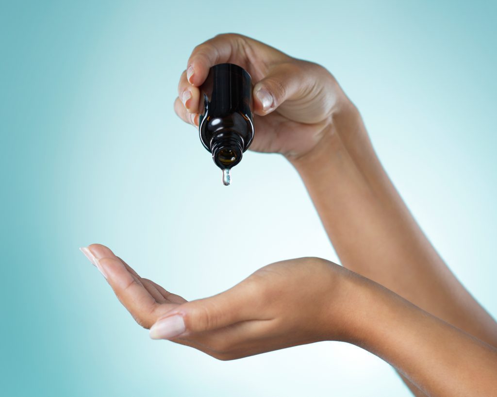 Shot of a young woman taking serum from a dropper against a grey background.