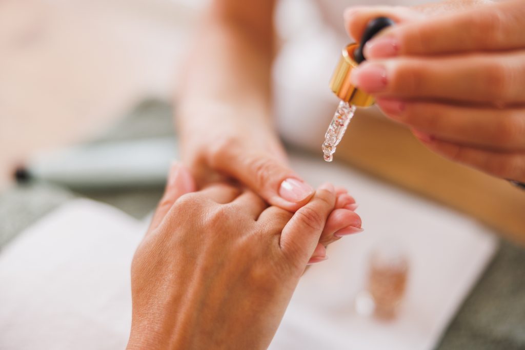 Cropped image of an unrecognizable woman getting esential oil treatment for cuticles during manicure.