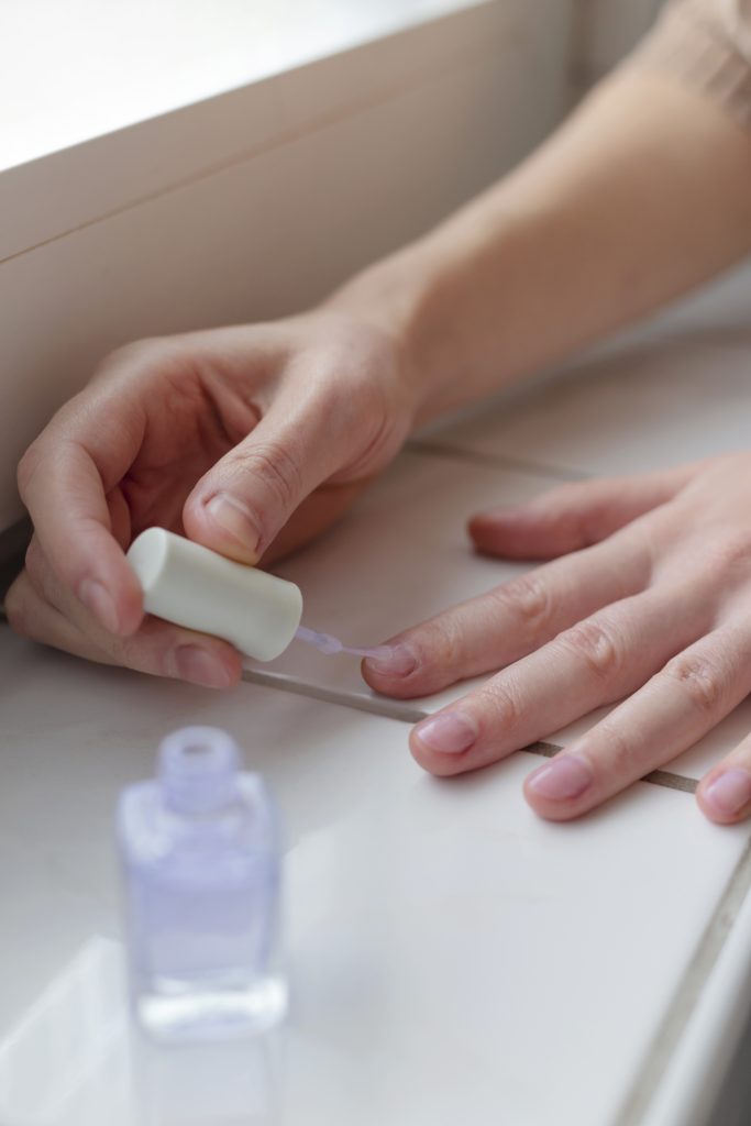 Woman paints her nails with transparent vegan nail polish.
