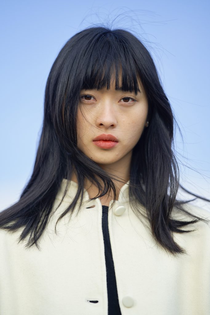 Woman with long black hair wearing a white coat against a clear blue sky. Brandenburg, Germany
