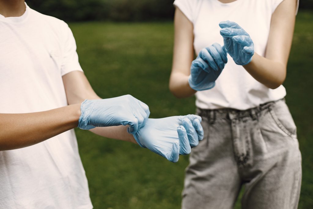 Unrecognizable boy and girl preparing for cleaning the rubbish outdoor. They are putting rubber gloves on.