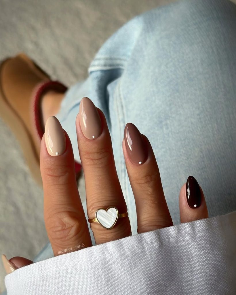 Teenager-friendly Almond nail shape tutorial image showing four natural nails filed into a perfect Almond shape. The nails are painted in a stylish gradient manicure using four shades of neutral and brown polish, each featuring a tiny white dot near the cuticle. This look highlights the slimming and lengthening effect of the Almond shape, perfect for readers trying elegant nail shapes at home.