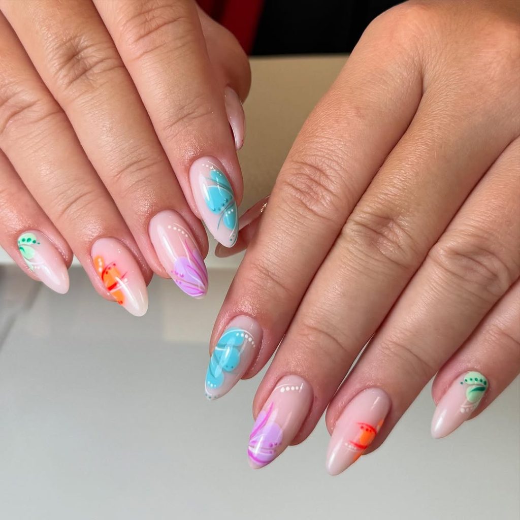 Two hands showing Oval nail shapes with a natural, medium length and a nude base coat. The nails feature bright, hand-painted watercolor butterfly and abstract floral designs in neon blue, orange, purple, and green. This image is a great example of fun nail art on almond or oval shapes that teenagers can recreate or take inspiration from when learning how to file nail shapes at home.