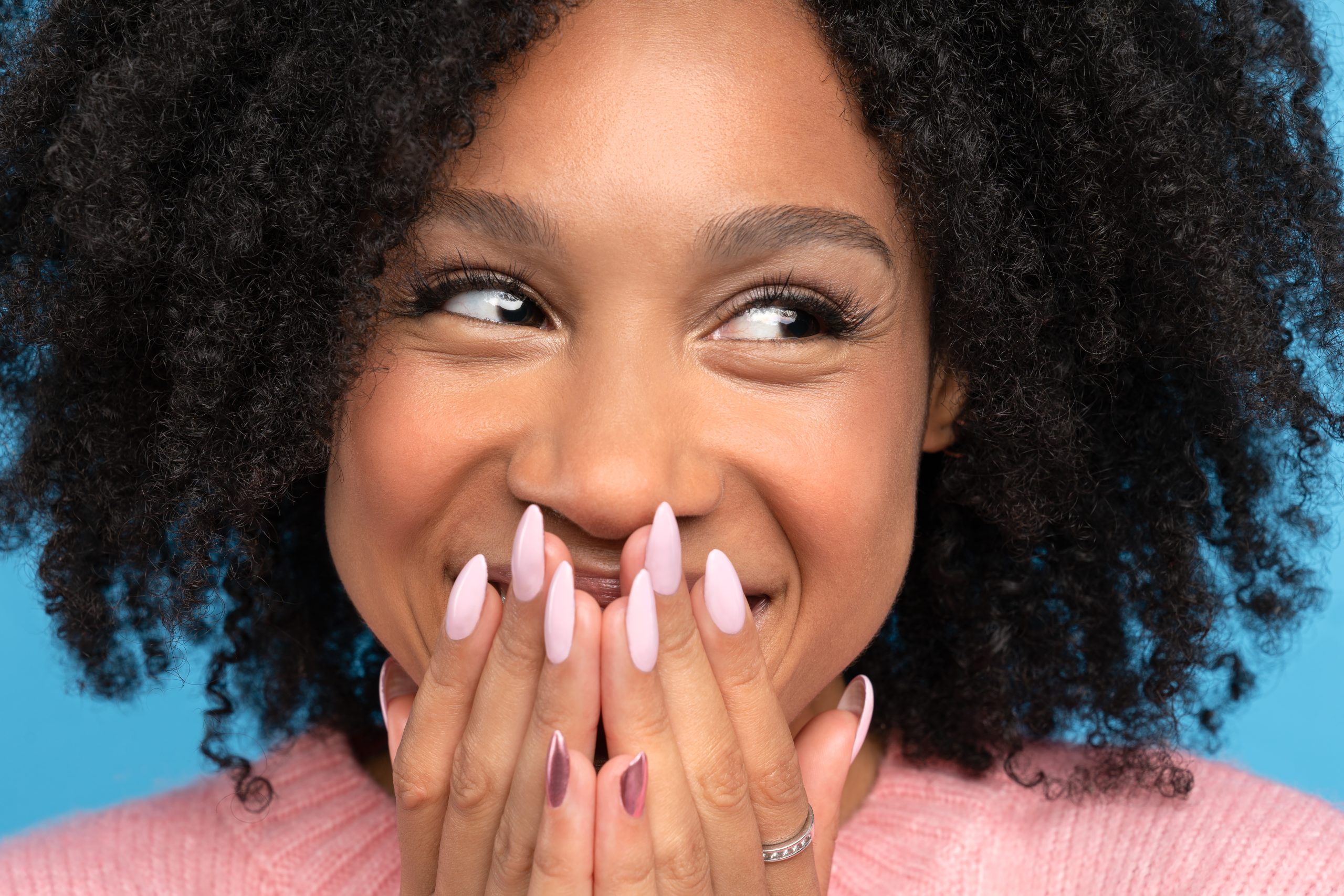 Teenagers Nail Shapes. Close-up studio portrait of a smiling teenager covering her mouth with her hands. Her long fingernails are perfectly filed into a dramatic Almond or Coffin nail shape and painted with a soft, glossy pale pink polish. This image showcases a trendy, long nail shape popular with teenagers and is an inspiring photo for the DIY Almond nail shape tutorial.