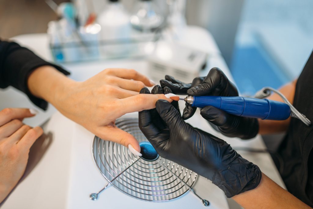 Beautician in black gloves sticks the nails of the client, manicure in salon. Manicurist doing hands care cosmetic procedure