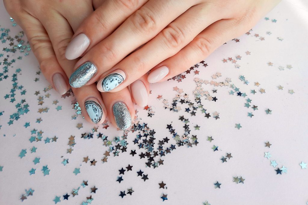 Beautiful female hand with Christmas nail design on pink background. Nail design, manicure with chimes pattern. Sequins. Shellac, gel polish.