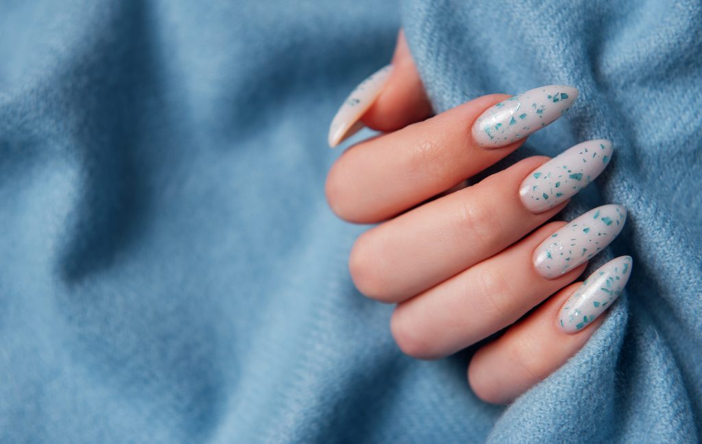 Female hands with blue nail design on blue textile background. Blue nail polish manicure.