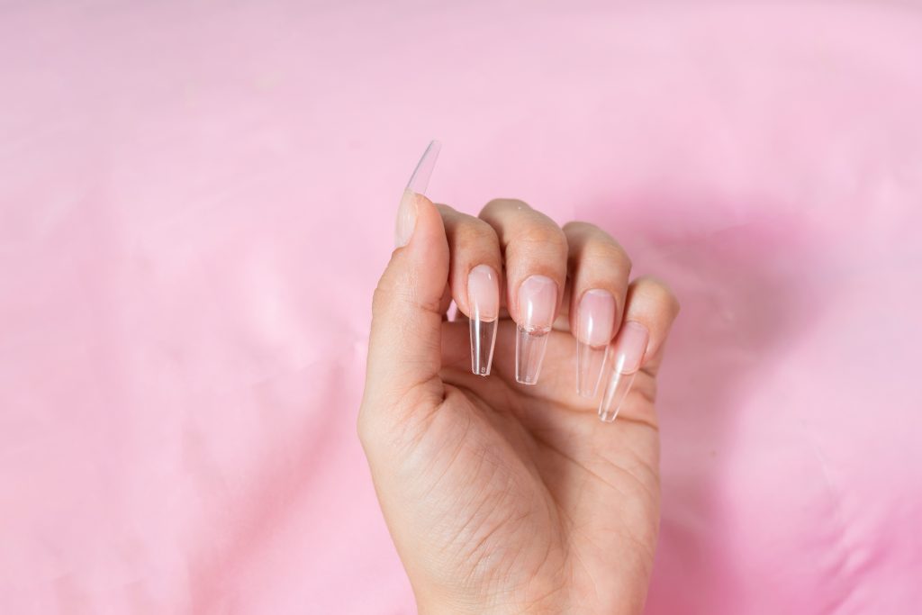 hand of a young woman on a pink background, with transparent false nails ready for a manicure. nail tips. nail form.