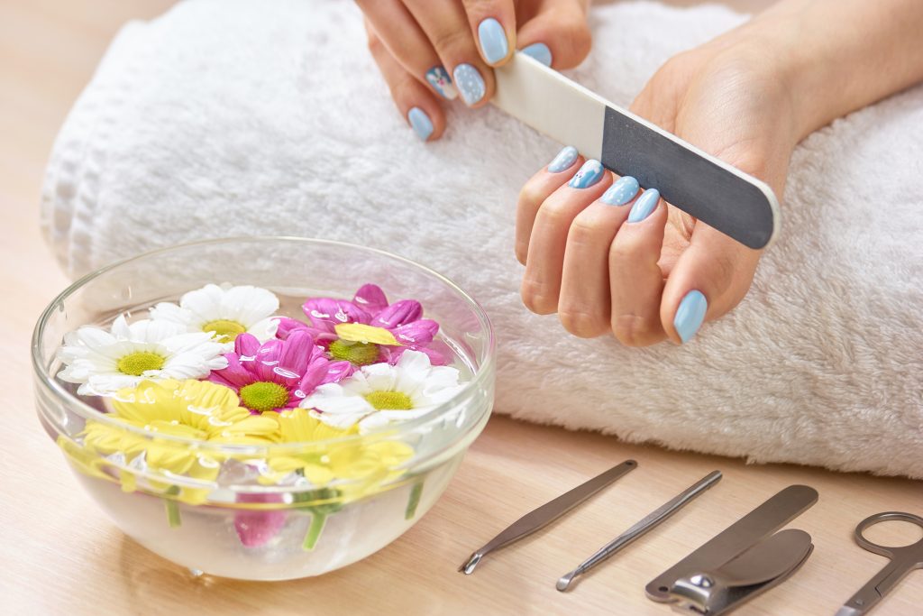 Woman filling nails on towel. Young woman hands in spa salon polishing manicured nails, bath for hands, manicure equipment.
