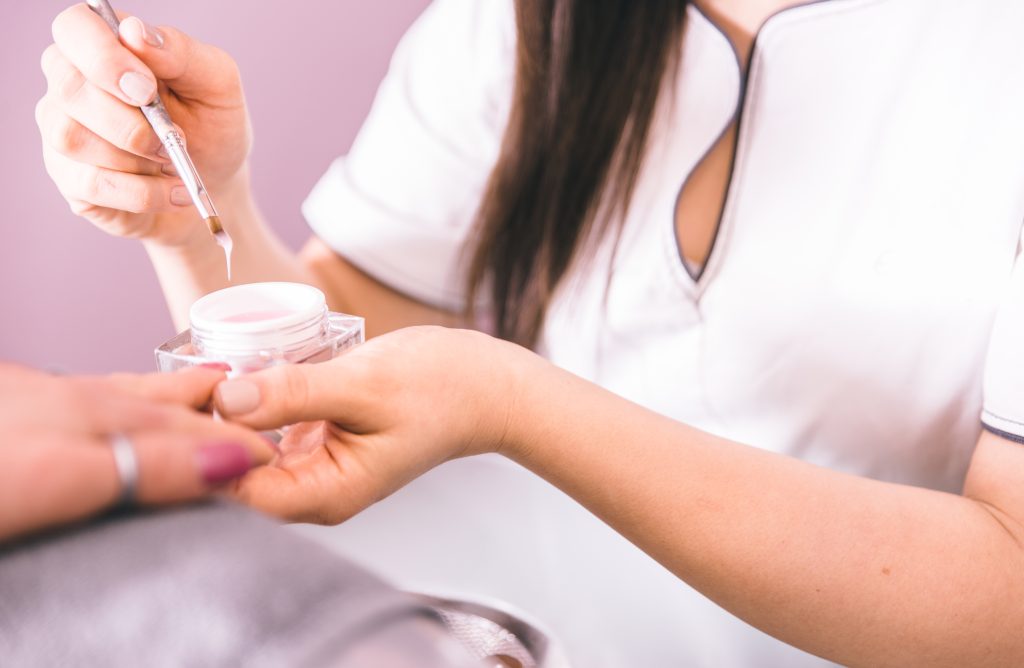 Acrylic Nails. Woman making nails treatment in a beauty saloon. Beautician working with the brusher. Beauty concept. Acrylic nails application in a professional nail salon.