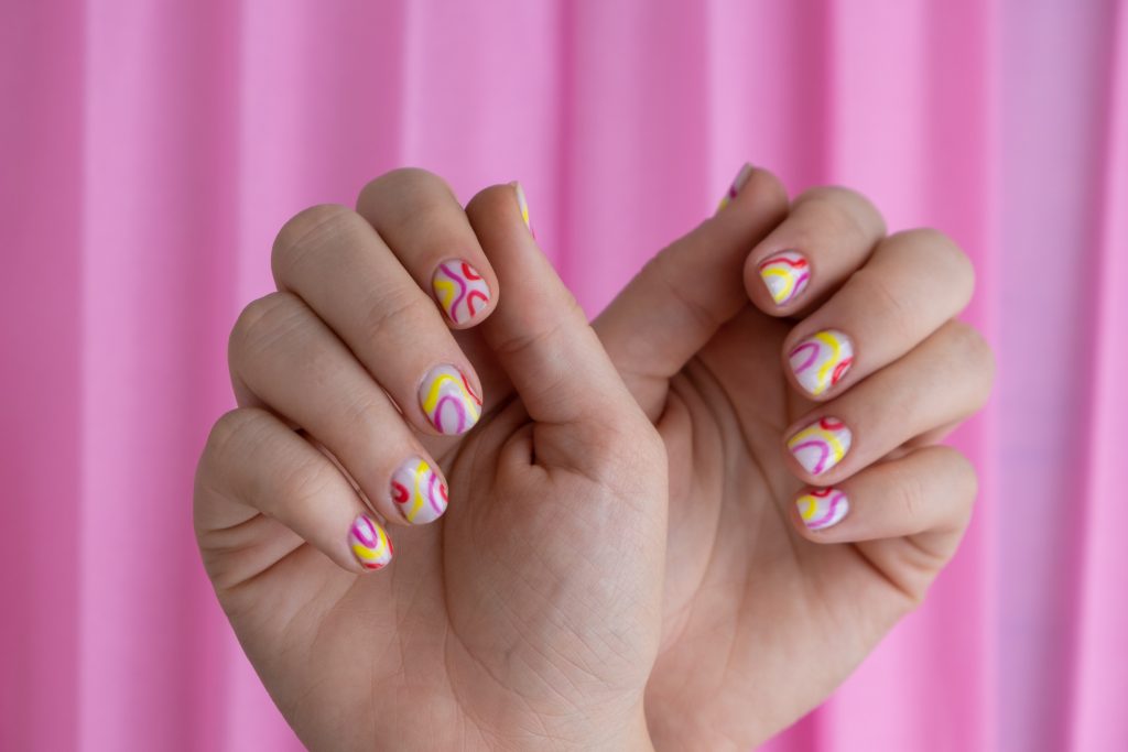 Woman manicured hands, stylish summer colorful nails on pink background. Closeup of manicured nails of female hand. Summer style of nail design concept. Beauty treatment.