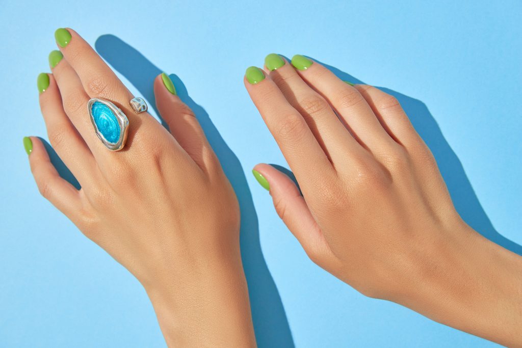 Womans hands with green manicure close up on blue background. Beauty treatment spa body care. Salon concept.