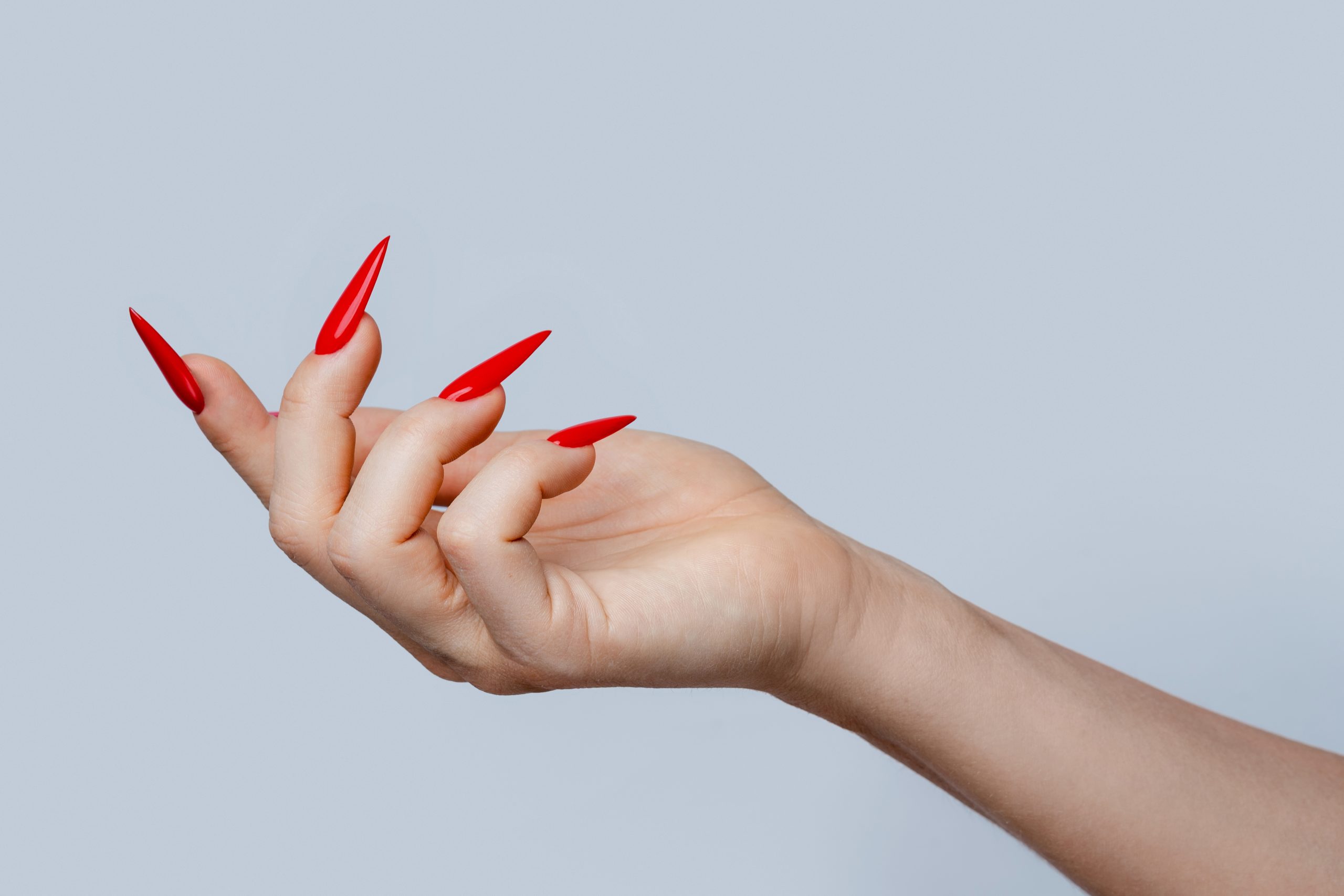 Stiletto Nails. 2025 Stiletto Nail Designs. Closeup of elegant female hand with red stiletto nails on gray background. ideas, inspiration, tutorial, trend forecast, home enthusiast, salon quality.