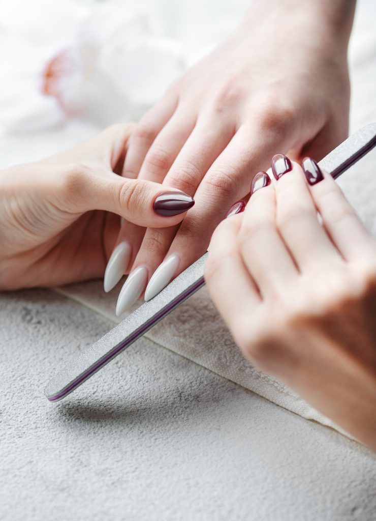 Nail technician using a precision file to shape a long white stiletto nail, illustrating essential 2025 stiletto nail maintenance and care tips.