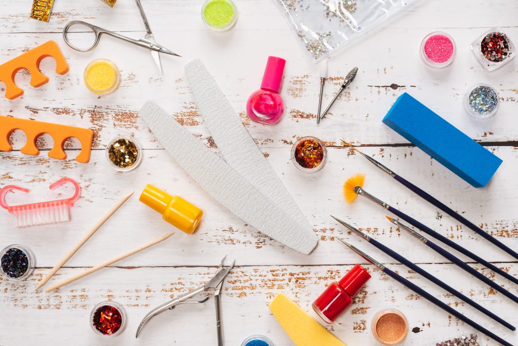 Flat lay of essential DIY stiletto nail tools, including precision files, glitter, brushes, and colorful gel polishes, to achieve salon-quality 2025 designs. 