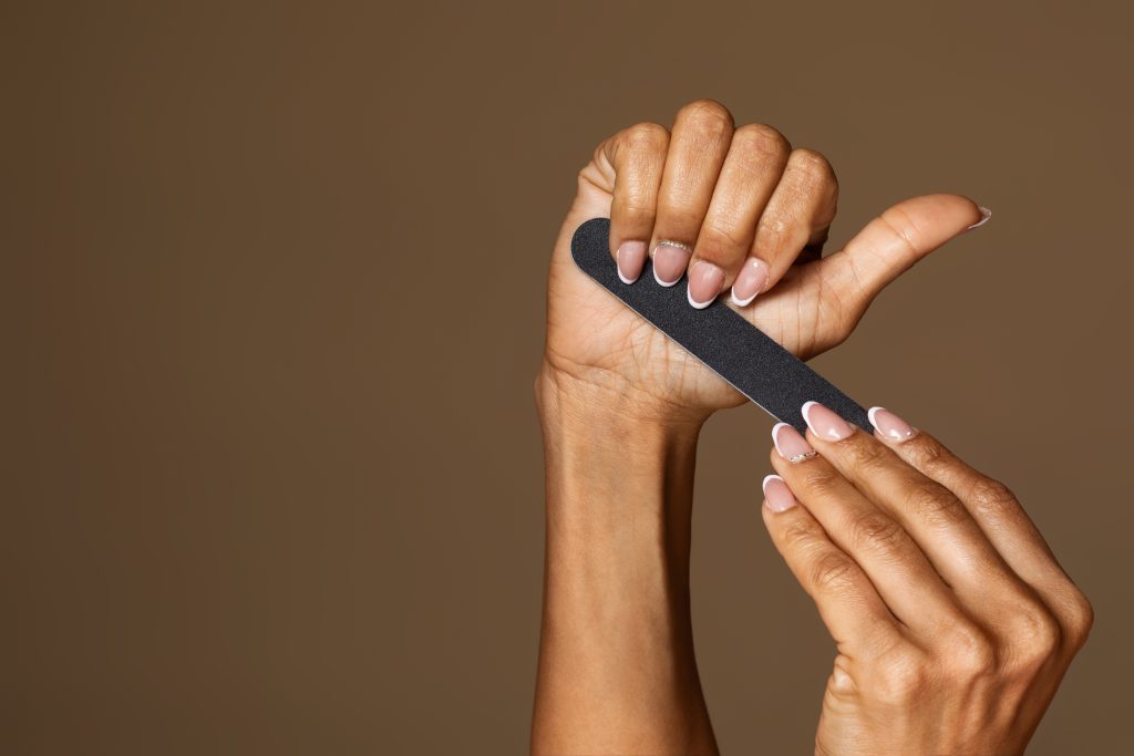 African american middle aged woman with manicure holding nail file isolated on brown studio background, free space, banner. Nail care concept