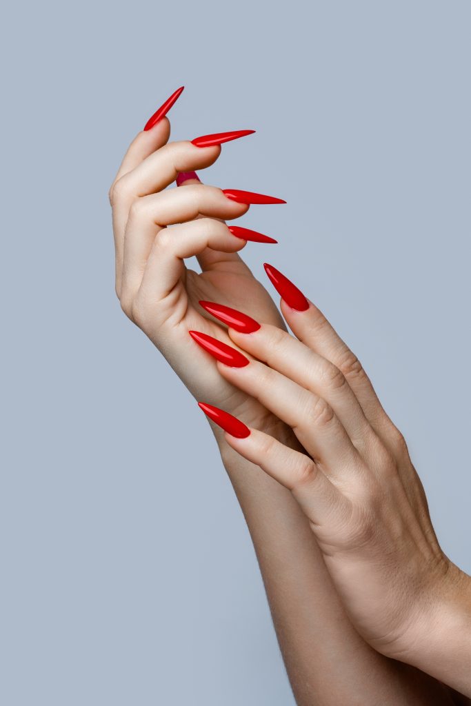 Closeup of  elegant female hands with red stiletto nails on gray background. Nail shape