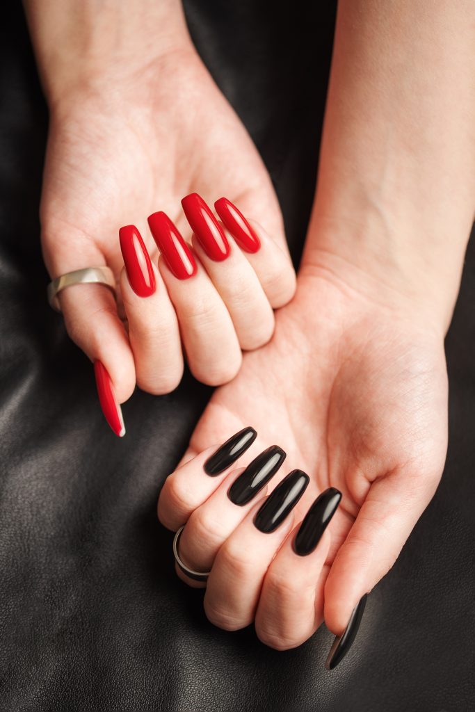 nail shape personality. Hands of young girl with black and red manicure on nails on black leather background. 2025 nail shape trends