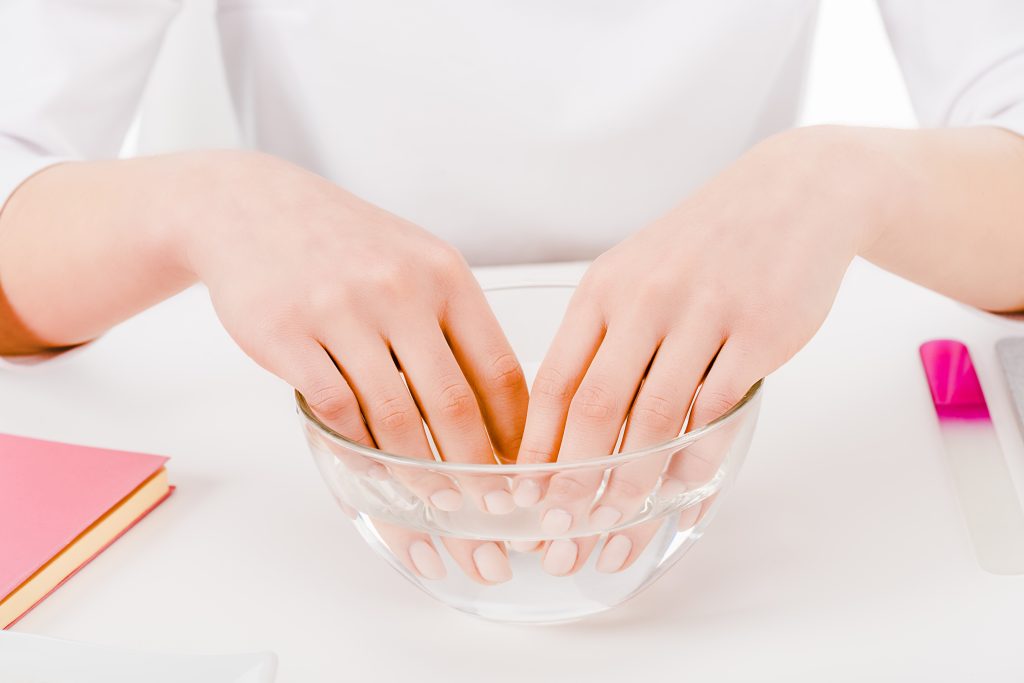 Partial view of a woman soaking her fingers in warm water and oil as an acetone-free method to remove polygel safely