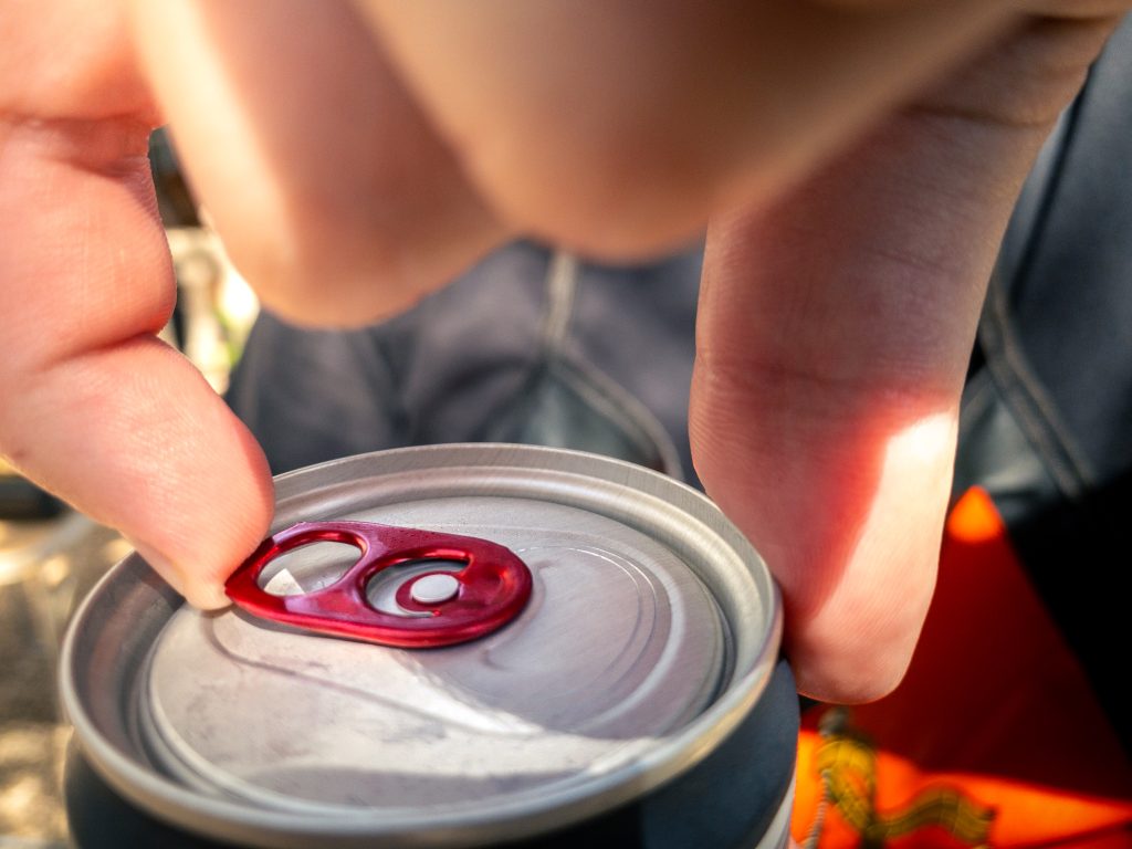 Closeup of hand man holding and opening pull tab of soda or beer can. Hands open a metal aluminum beverage drink cola can with natural sunlight at outside