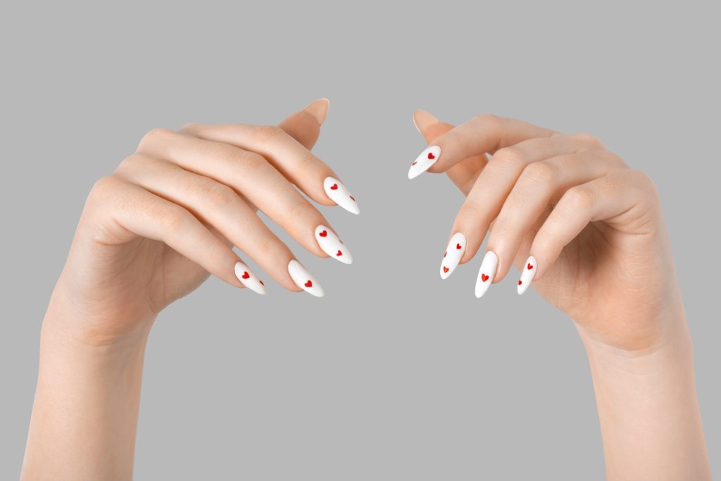 Female manicure two hands minimal gel polish white long nails and red hearts desing gray isolated background. Beauty spa, Valentine's Day, love concept