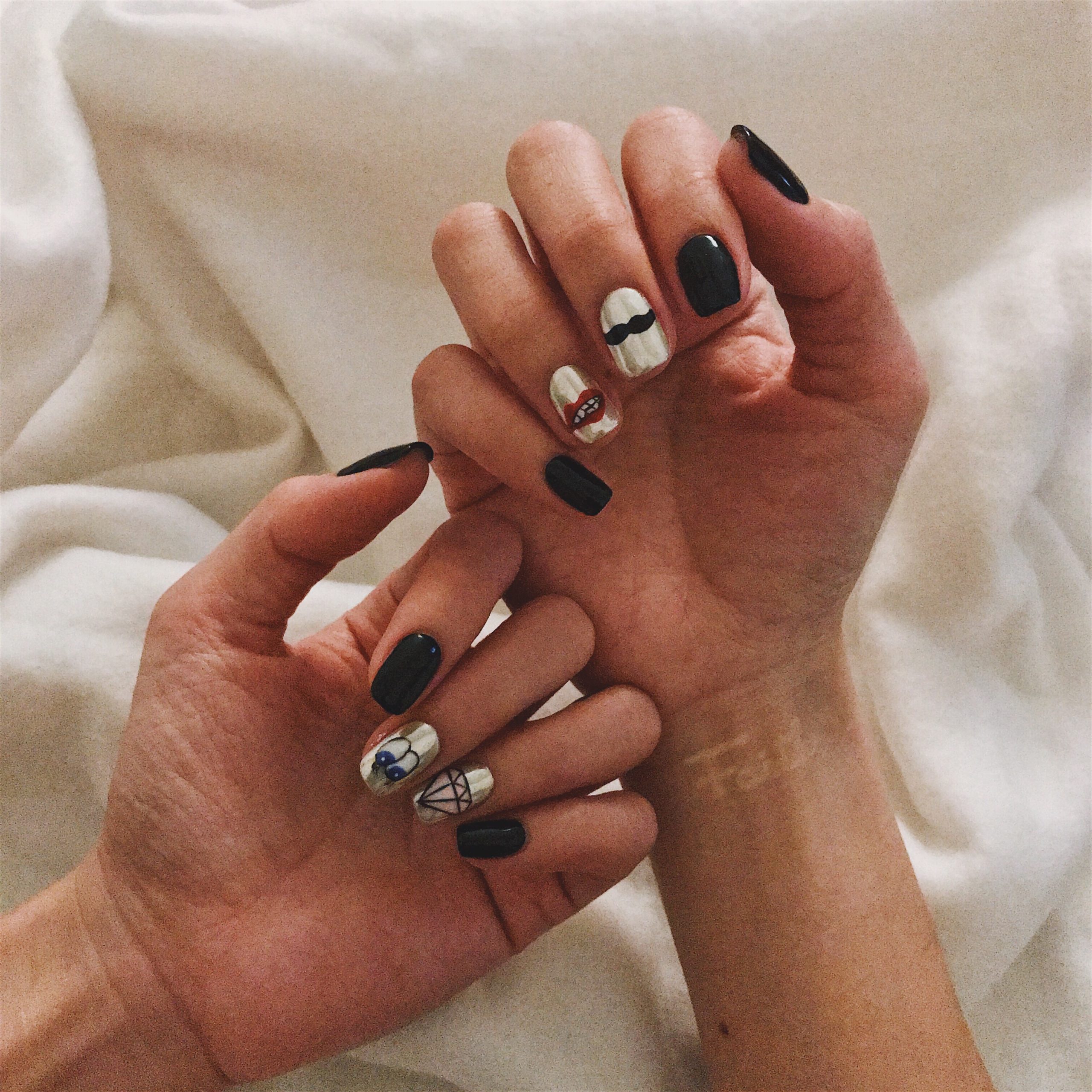 A whimsical and fun simple 2026 Nail Art Ideas featuring black matte polish, silver metallic accents with red lips and mustache icons, a diamond shape, and a black eye detail on a white background.