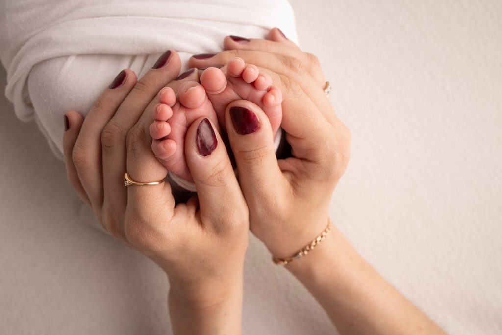 Mother is doing massage on her baby foot. Closeup baby feet in mother hands. Prevention of flat feet, development, muscle tone, dysplasia. Family, love, care, and health concepts. Studio macro.