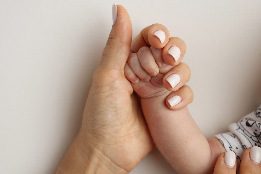 Parents' hands hold the fingers of a newborn baby. The hand of a mother and father close-up holds the fist of a newborn baby. Family health and medical care. Professional photo on white background.