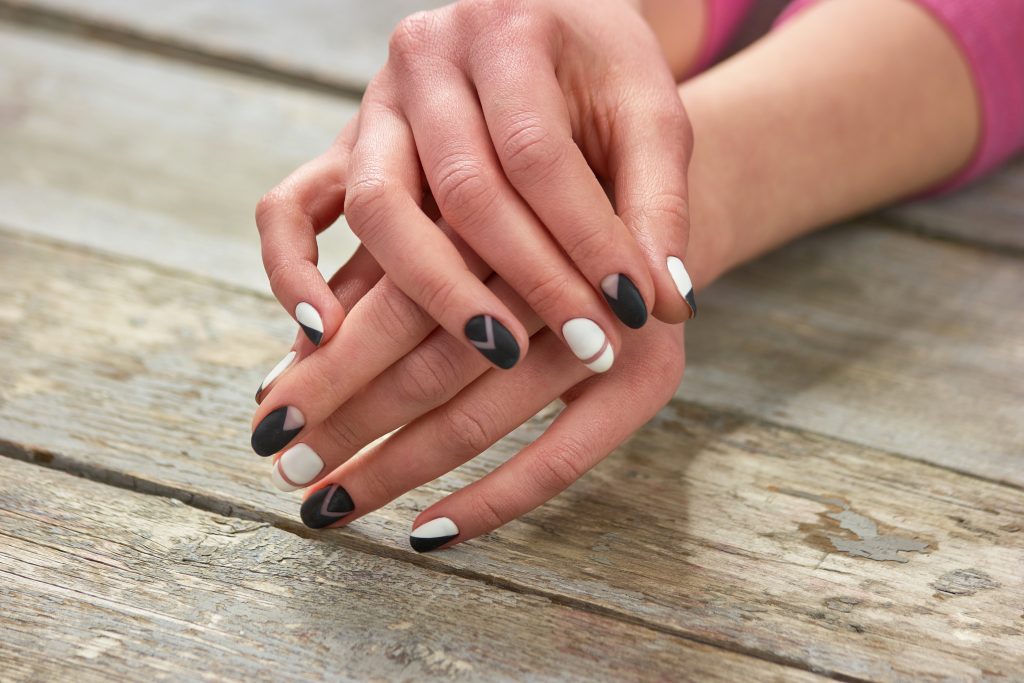 Woman hands with stylish manicure. Creative black and white manicure on female hands, old wooden background. Nail Shapes for Moms.