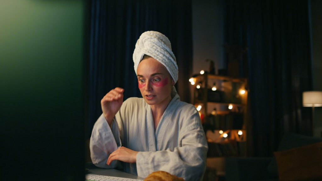Smart lady talking computer at night home closeup. Domestic woman talking virtual call at dark room while doing night skincare routine. Facial night care routine.