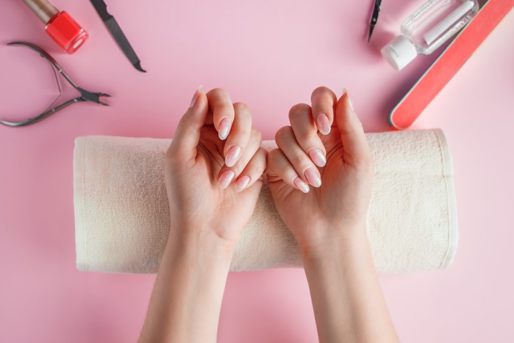 Nail care procedure in a beauty salon. Female hands and tools for manicure on a pink background. Concept spa body care.