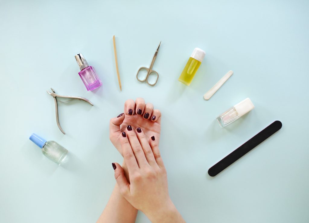 Top view of crop anonymous female with dark manicure sitting at table with various tools during professional manicure procedure in spa salon