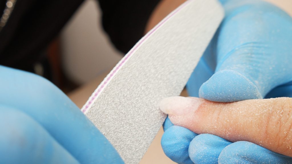 Manicurist files the shape of the nails with a special nail file, close up view. The manicurist shapes the nails with a nail file. The process of nail care in a beauty salon. Nail file processing.