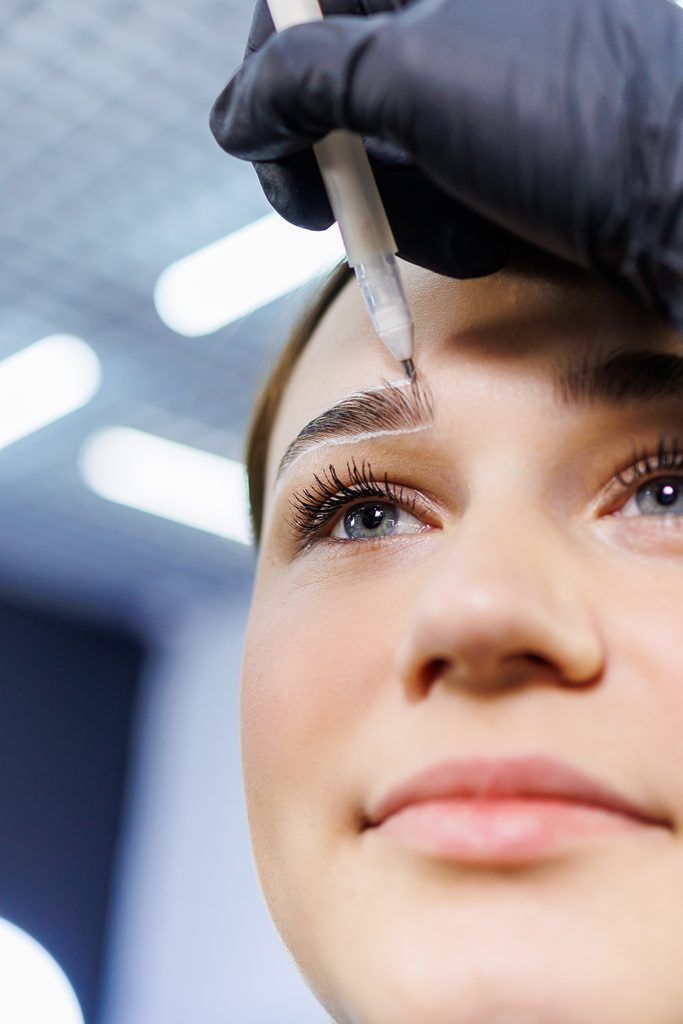 The master marks the woman's face before permanent eyebrow makeup. Eyebrow tattoo. Beauty procedure for a woman's face