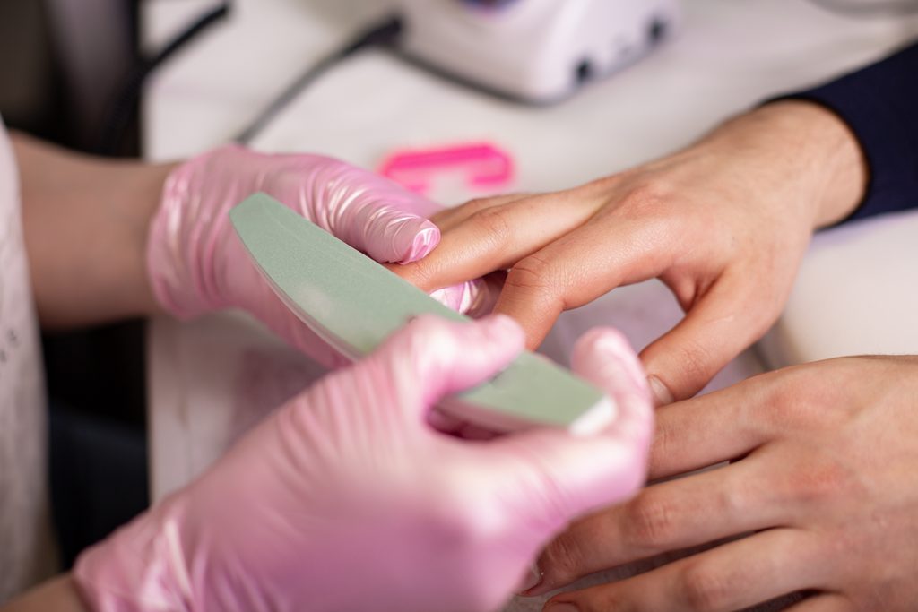 Close-up Of A Manicurist Filing Person's Nails In Salon. Nail buffer