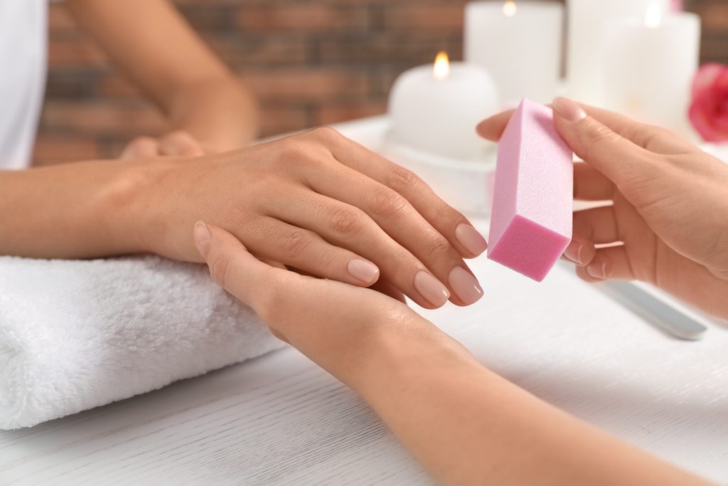 Manicurist polishing client's nails with buffer at table, closeup. Spa treatment. Nail buffer.