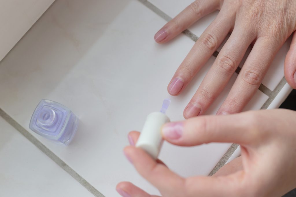 Woman paints her nails with transparent vegan nail polish. Eco self care. Care for Your Natural Nails After Removing Press-Ons.