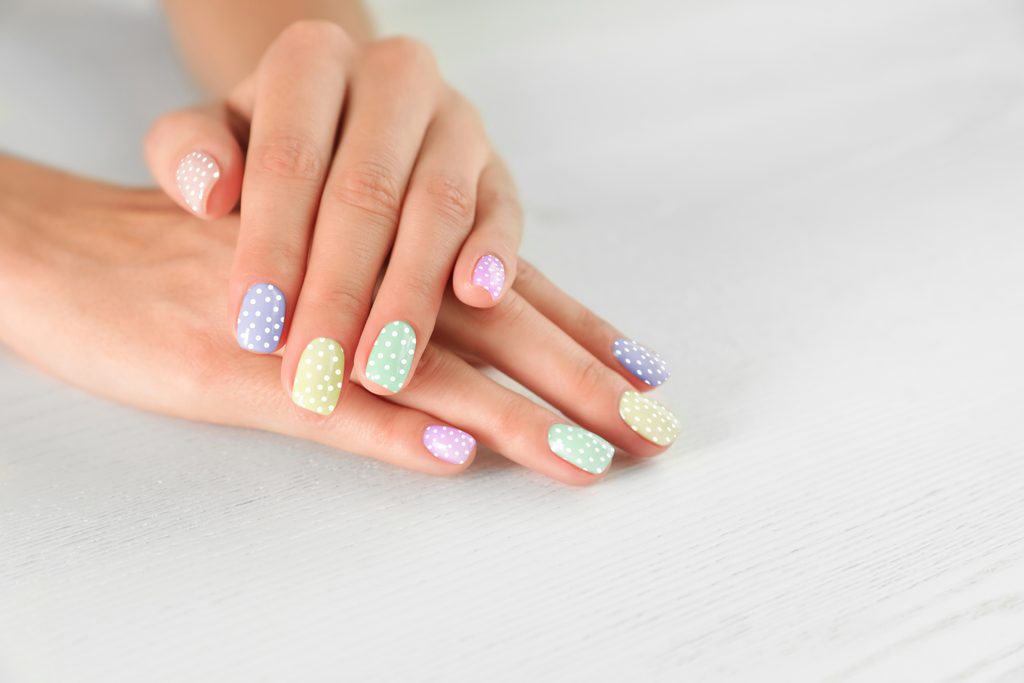 Woman showing her stylish colorful manicure on light background, closeup