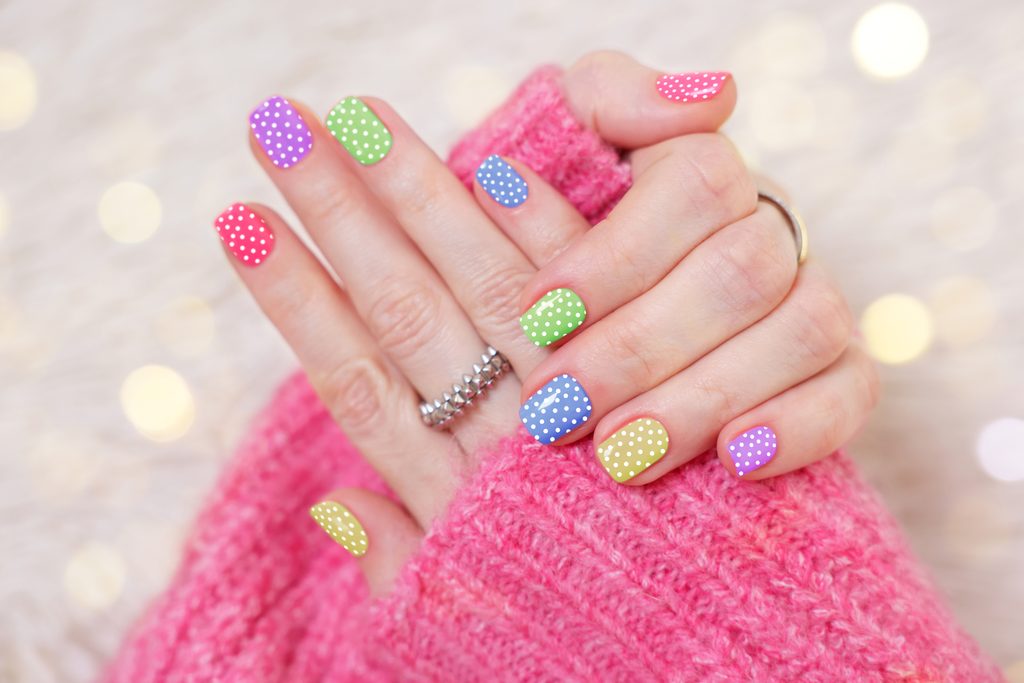 Woman showing her stylish colorful manicure on shiny background, closeup