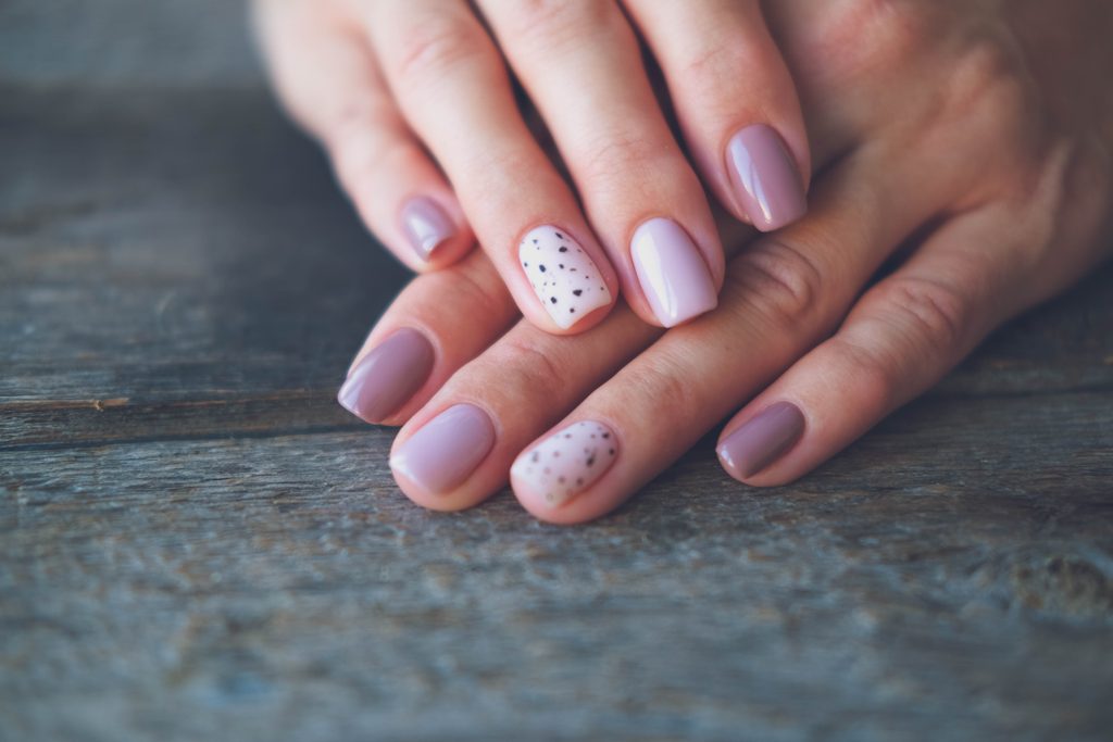Women is hands with a beautiful manicure on a wooden background. Autumn trend, polish the beige and quail egg pattern on the nails with gel polish, shellac. Copy space.